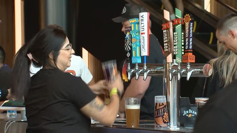 Server at the Footprint Center in Phoenix, Arizona pours beer for fans attending a Suns game.