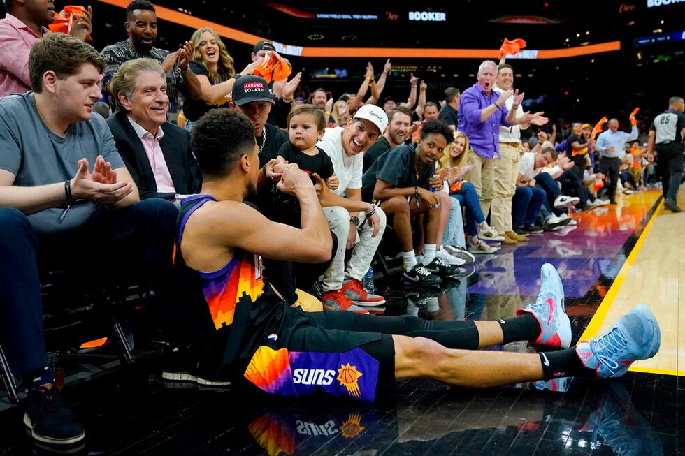 Phoenix Suns guard Devin Booker fist-bumps a young child after falling out of bounds while...