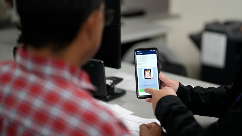 FILE - An officer helps set up a phone that will be used to track a man at an immigration and...