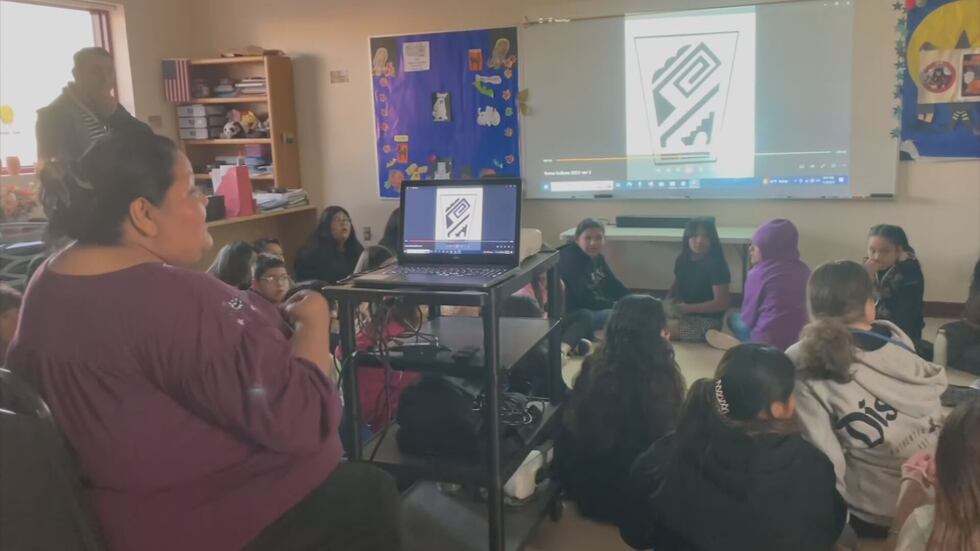 A teacher is giving a lesson to kids inside of a classroom with an image from a projector on a...